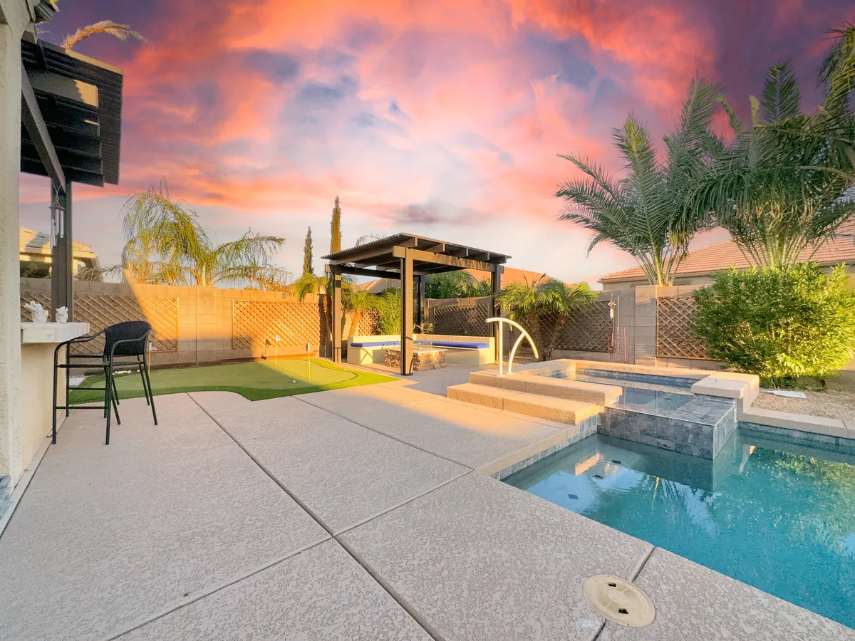 A luxurious backyard scene showcasing a sparkling swimming pool with an attached jacuzzi, surrounded by a comfortable outdoor seating area and a stylish gazebo, all set amidst lush greenery. The ambiance is warm and inviting, perfect for both daytime fun and cozy evening gatherings.