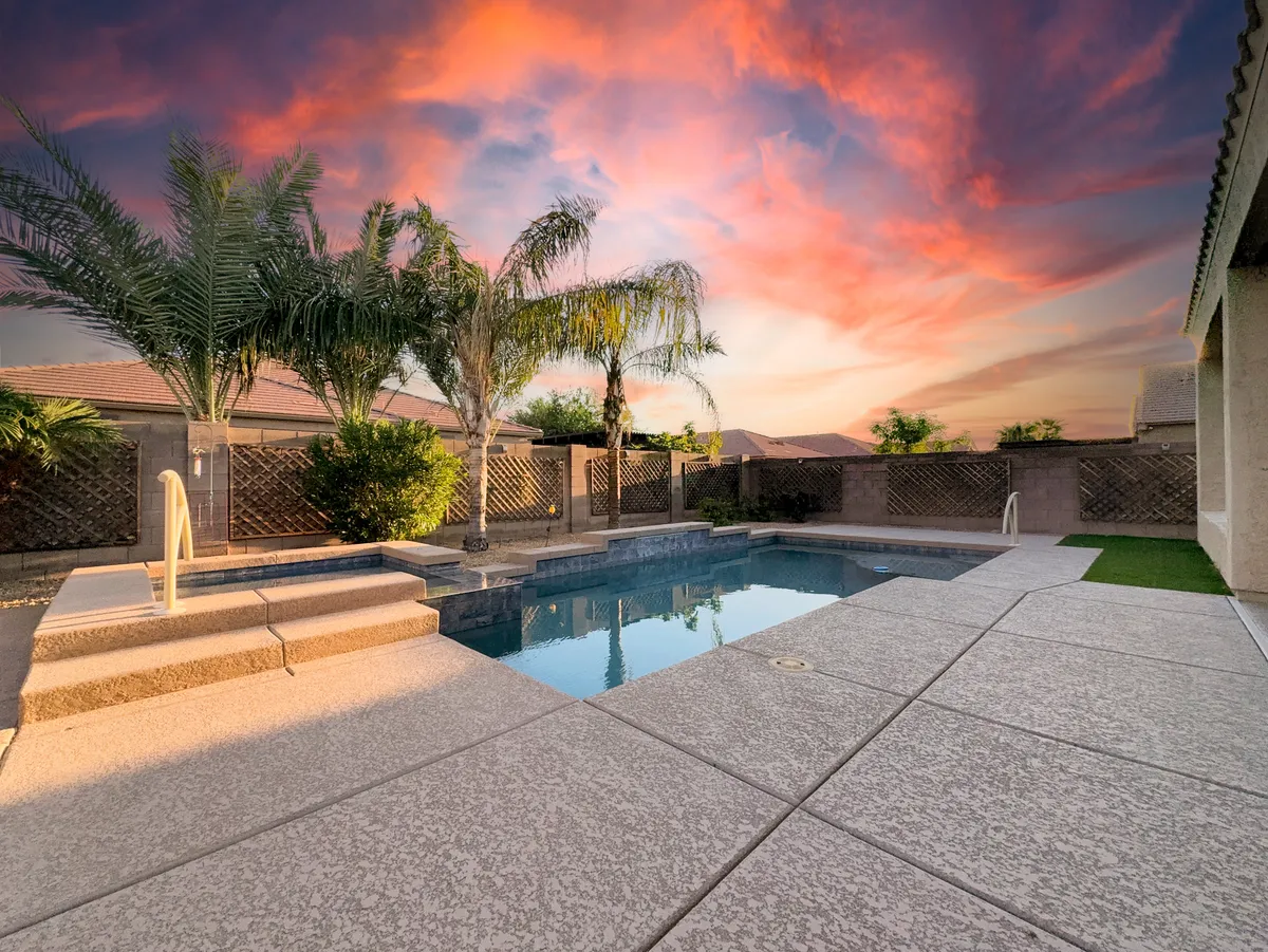 A tranquil backyard scene with a swimming pool, palm trees, and a stunning sunset sky. The open space is perfect for unwinding after a day of exploration, and the lush setting offers ample room for dogs to roam safely.