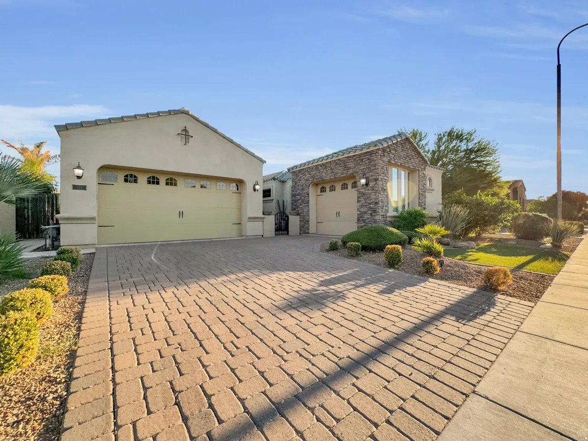 A welcoming exterior shot highlighting the front driveway, a two-car garage, a stone accent wall, and a landscaped garden. The well-maintained yard and ample driveway space suggest a neighborhood ideal for outdoor strolls and playful exploration with pets and children.
