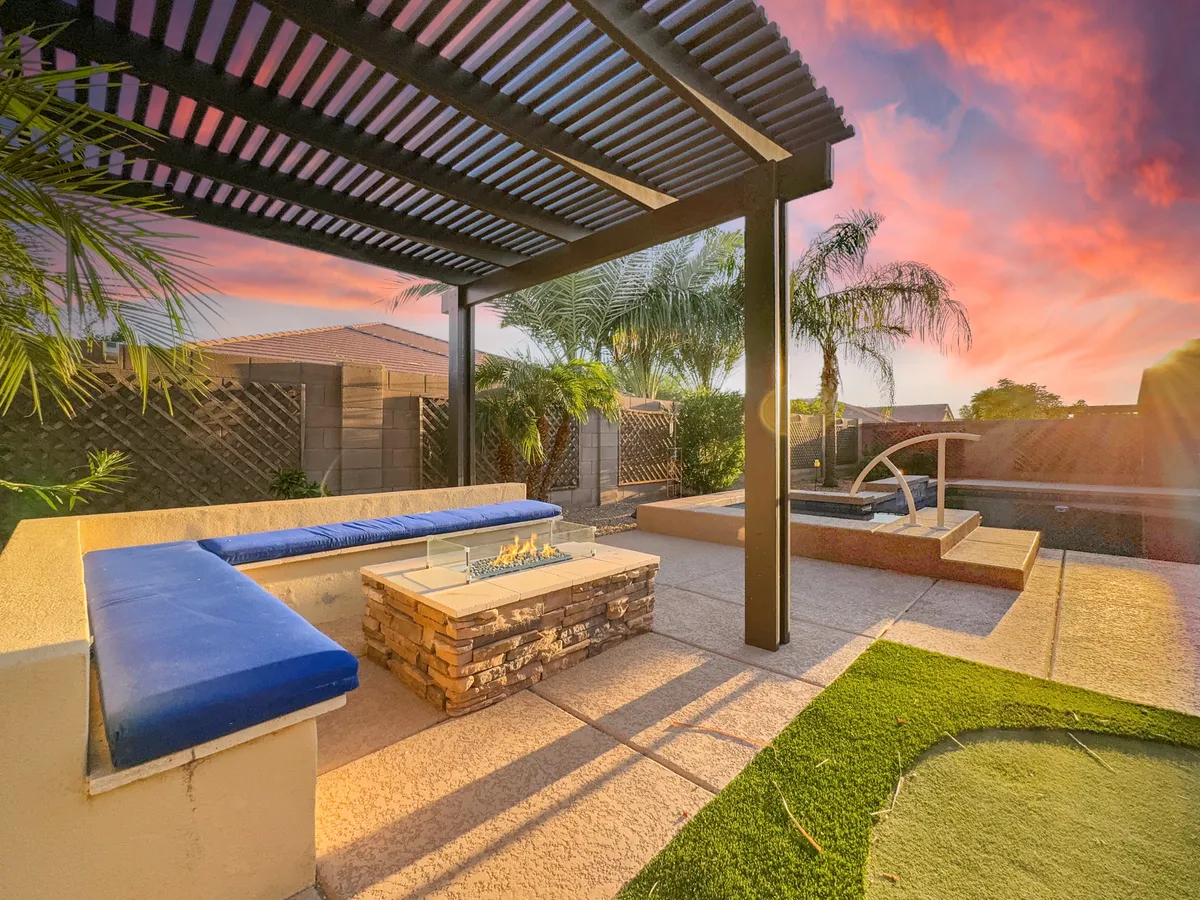 A cozy outdoor fire pit area with comfortable seating, palm trees in the background, and a gentle water feature. The ambiance is perfect for evening gatherings or stargazing by the fire.