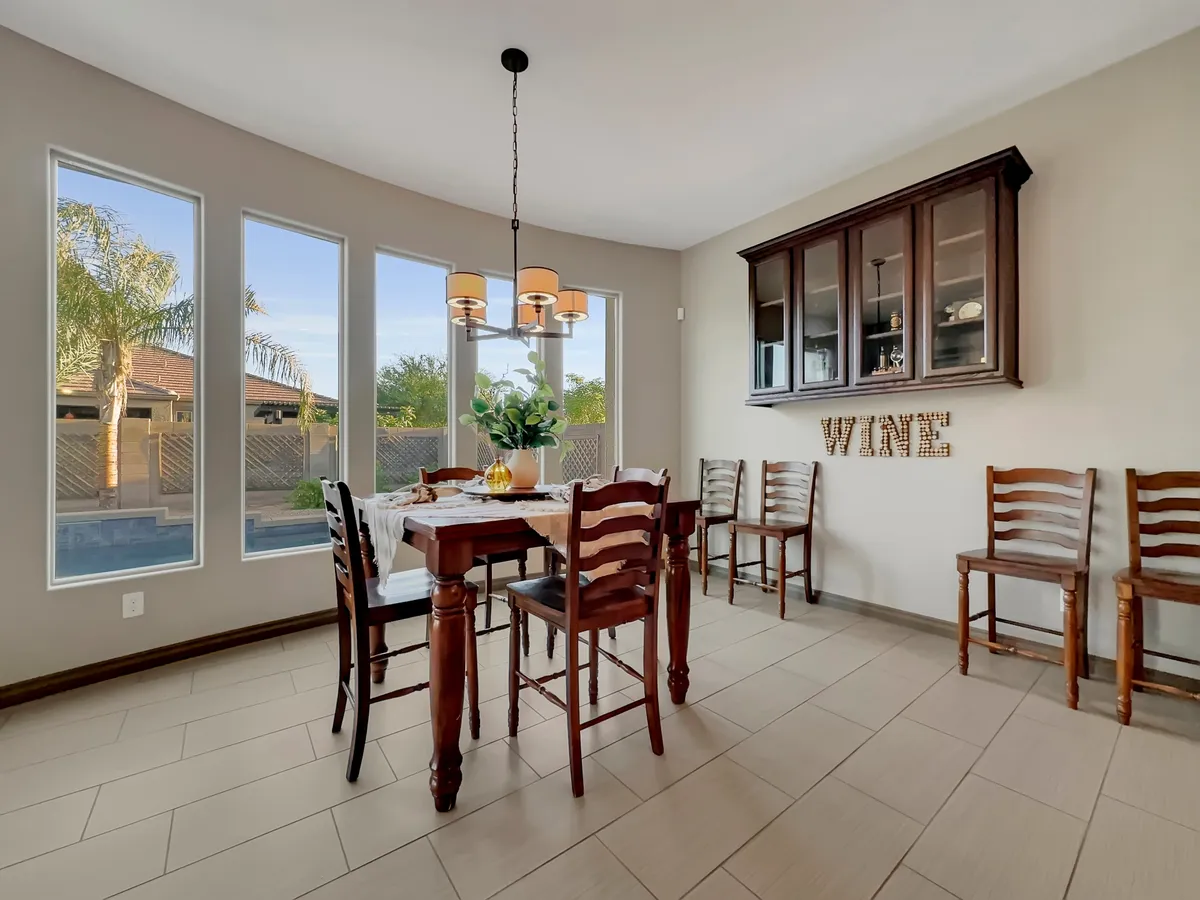 A cozy dining room is shown with a large table, elegant chandelier, and windows that fill the space with natural light. A wine display adds a touch of sophistication, while the setting invites shared meals and conversations.