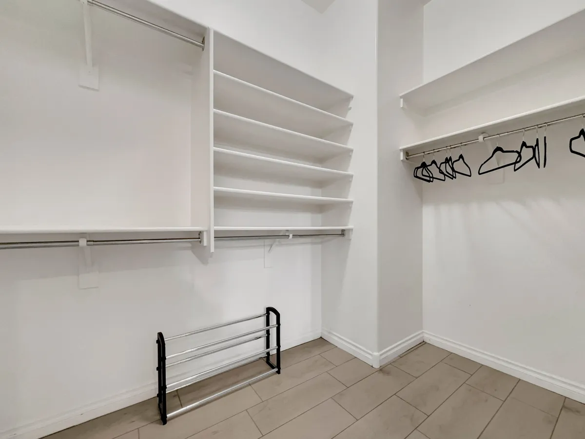 A spacious, well-organized closet with shelves, a hanger rod, and a folding rack, offering ample space for clothing and accessories. The minimalistic design emphasizes practicality and ease of use.