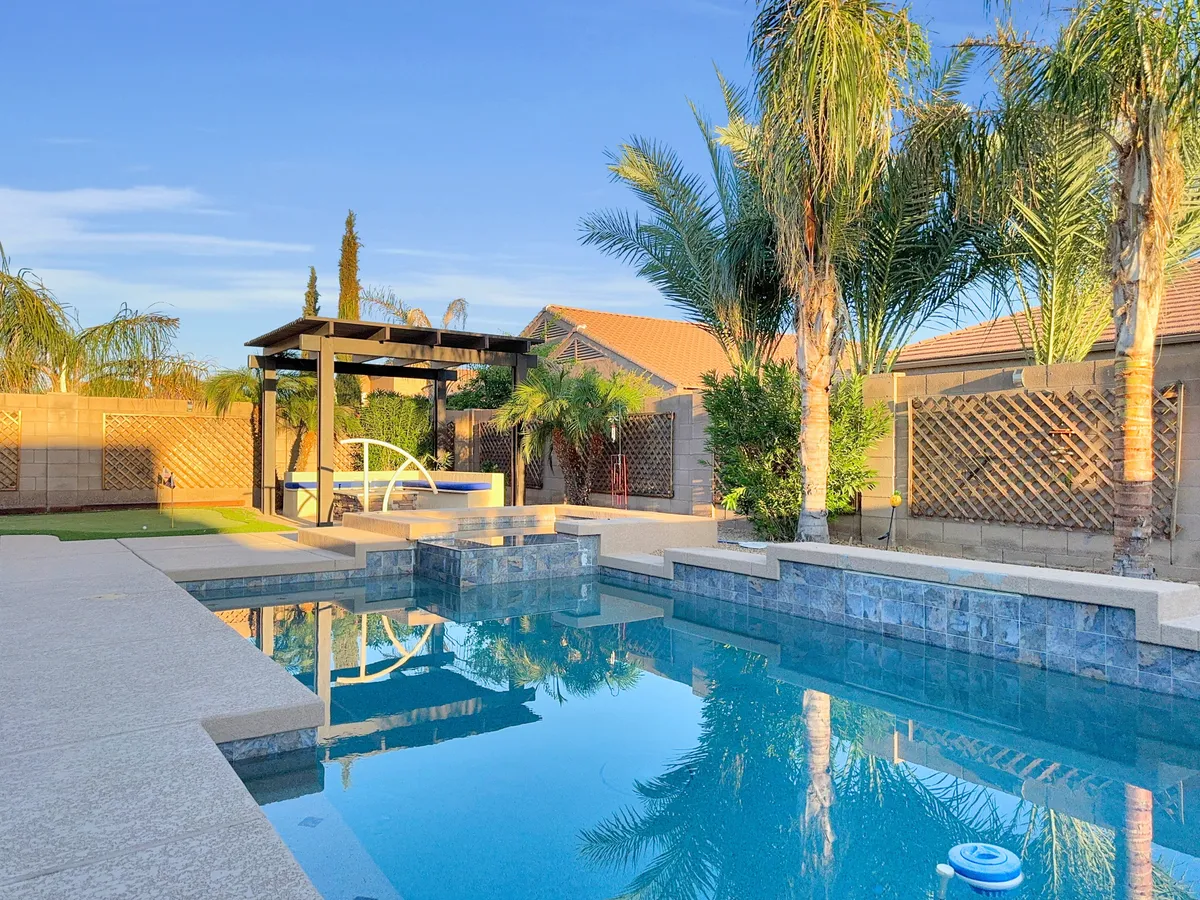 A spacious backyard featuring a sparkling swimming pool, tall palm trees, an inviting outdoor seating area, and a dedicated spa zone. The setup is perfect for both swimming and lounging, with enough space for family fun and gatherings.